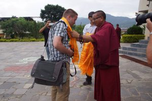 Ein Lama überreicht in einem Kloster einem Besucher einen Schal