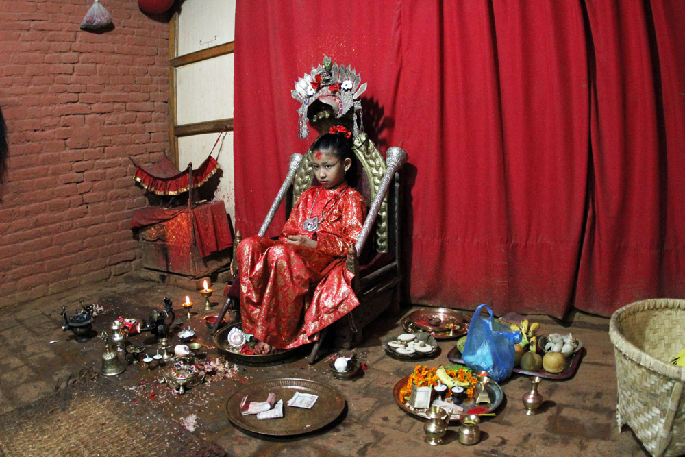 Die Kumari von Patan bei Kathmandu sitzt auf ihrem Thron und schaut traurig während Touristen sie besuchen