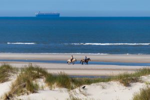 Am Strand von Wangerooge reiten zwei Reiter auf ihren Pferden