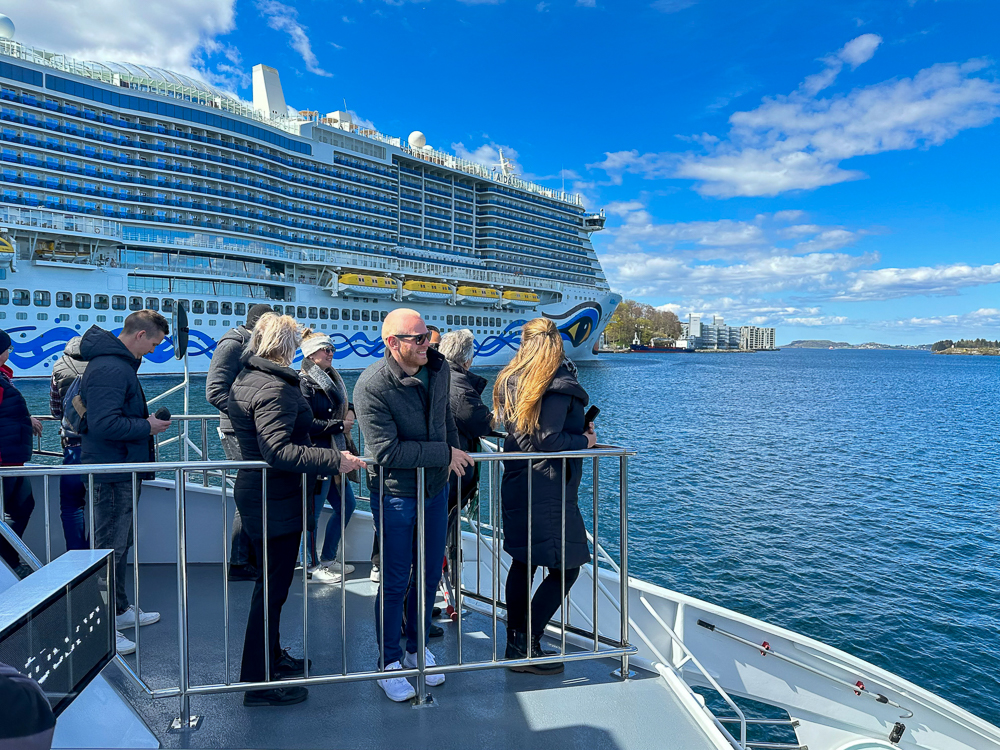 Ausflug mit einem Katamaran von Stavanger über den Lysefjord zum Preikestolen. Im Hintergrund ist das Kreuzfahrtschiff AIDAnova auf einer Kreuzfahrt durch Norwegen zu sehen.